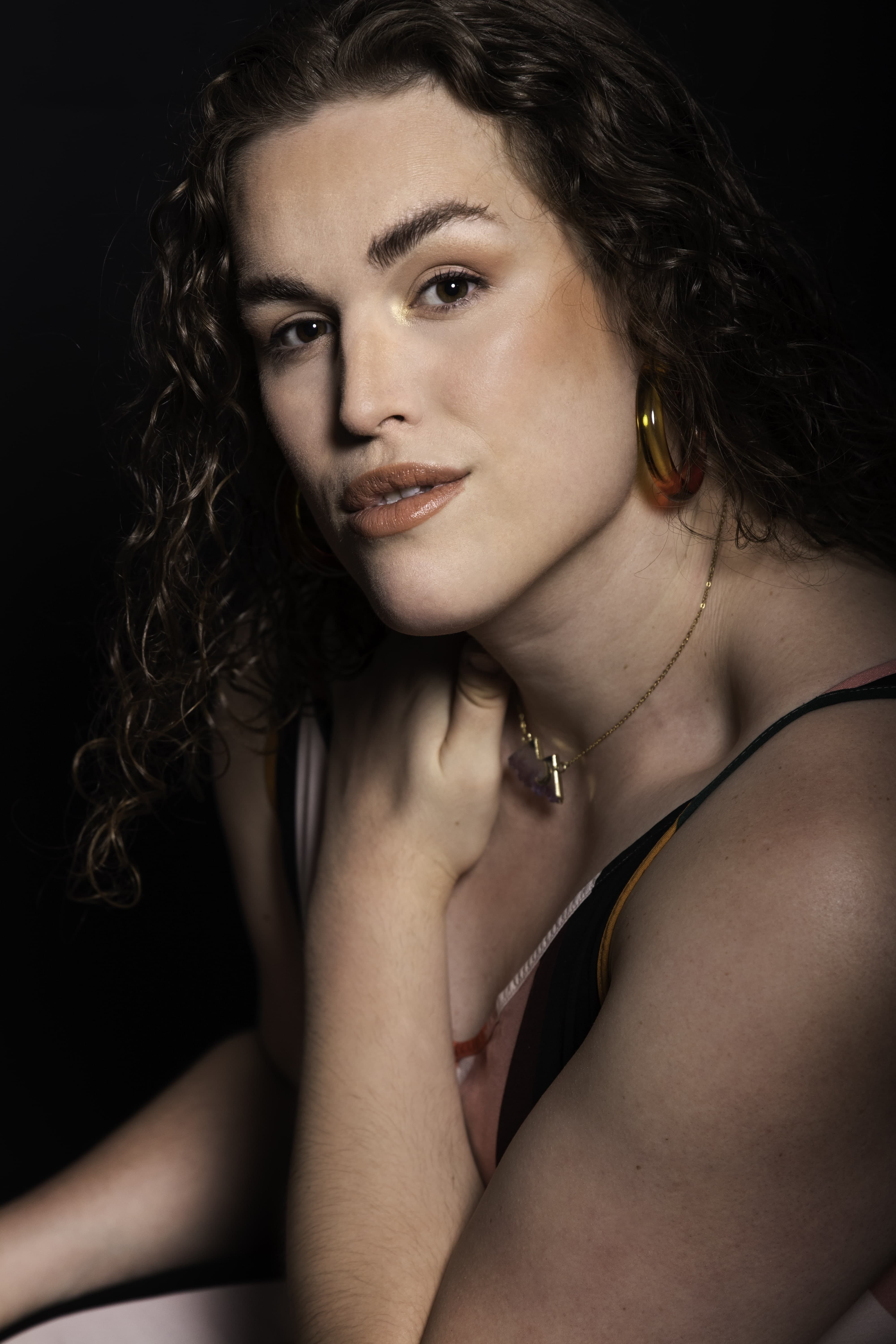 Woman with hand across chest and holding shoulder looking directly at camera