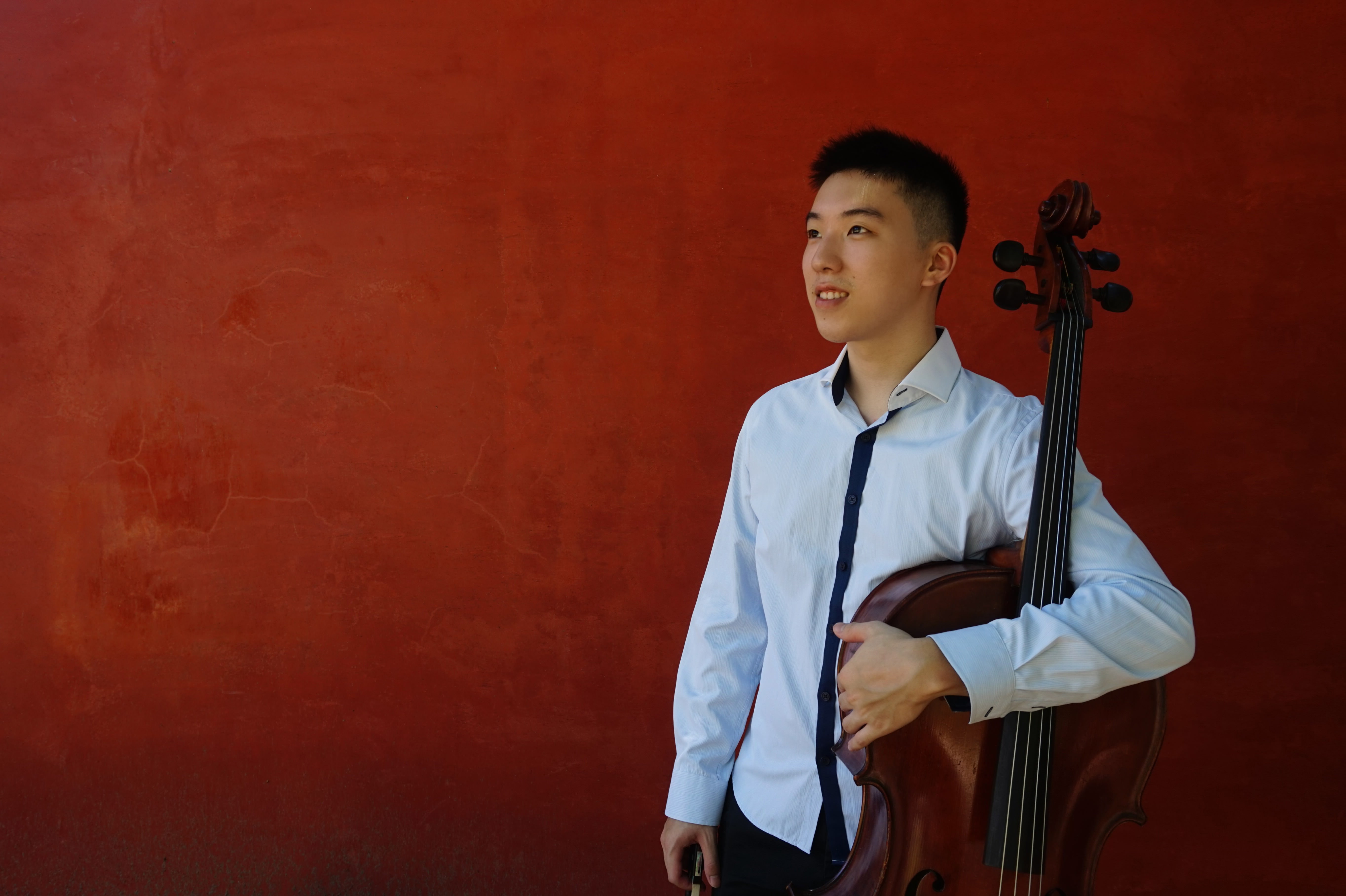 Man holding cello and standing against red wall
