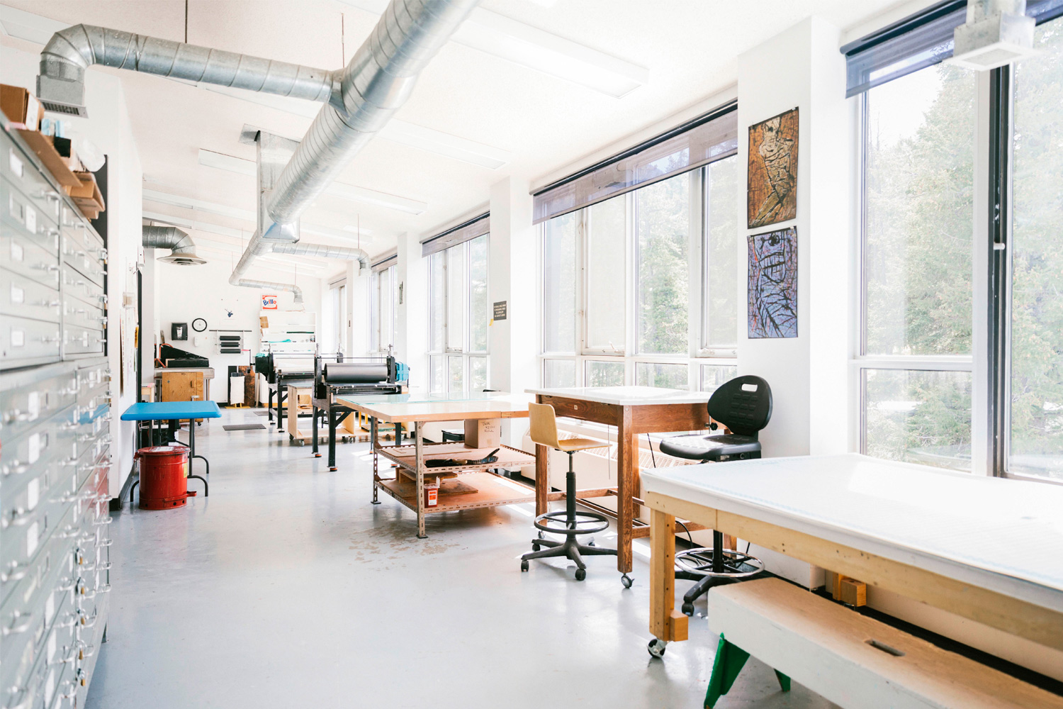 brightly lit artist studio with large windows and tables. 