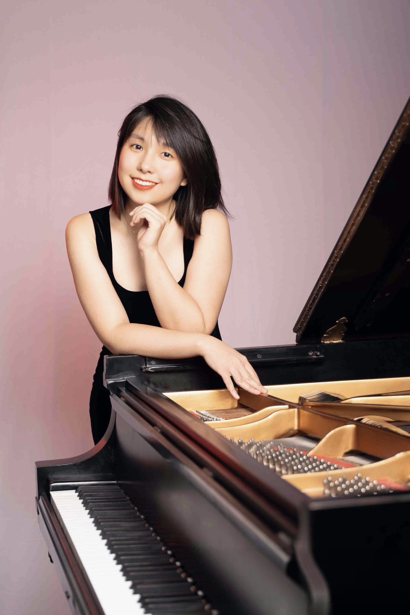 Woman leaning over piano smiling in black dress