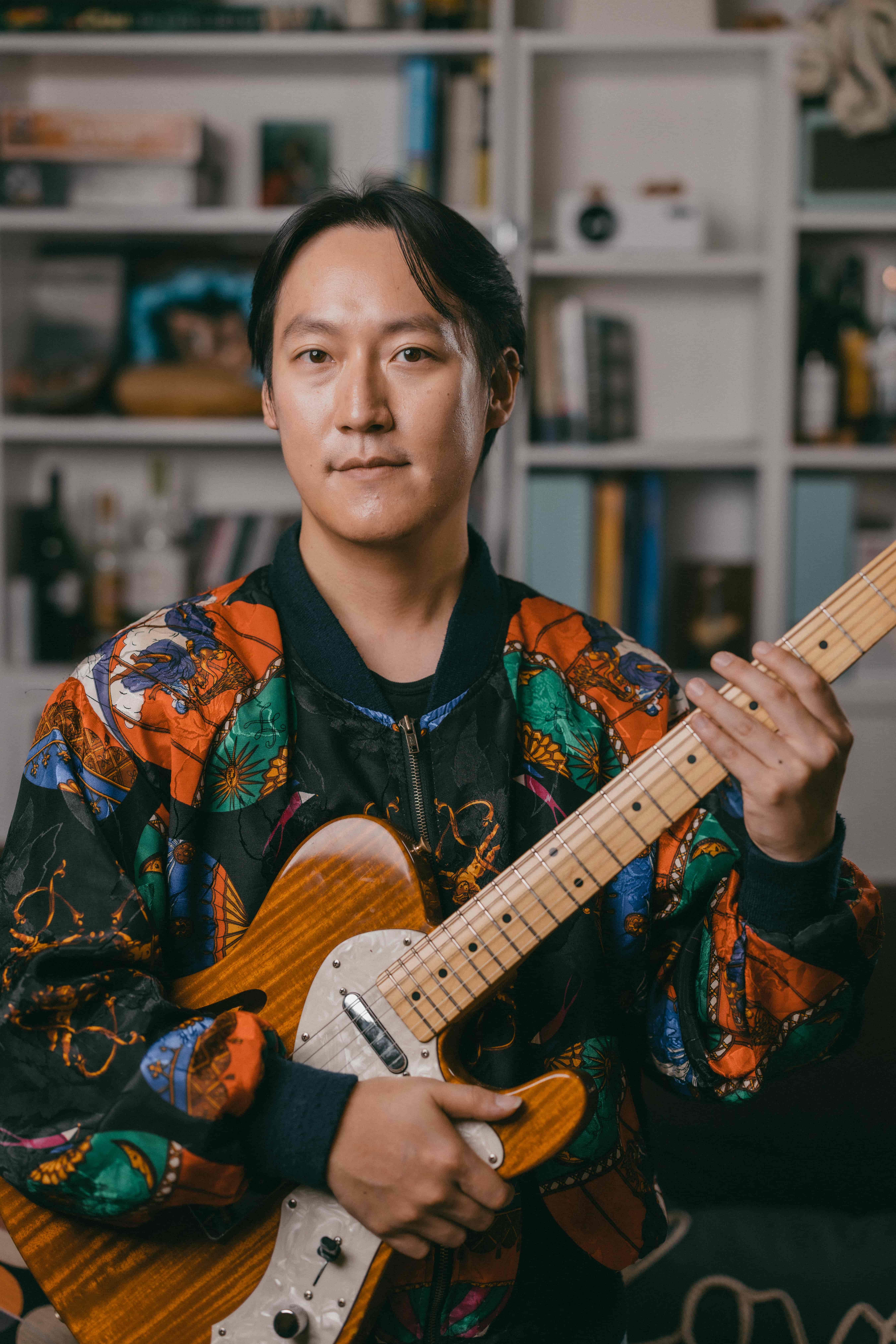Man holding string instruments with colourful jacket on looking at the camera