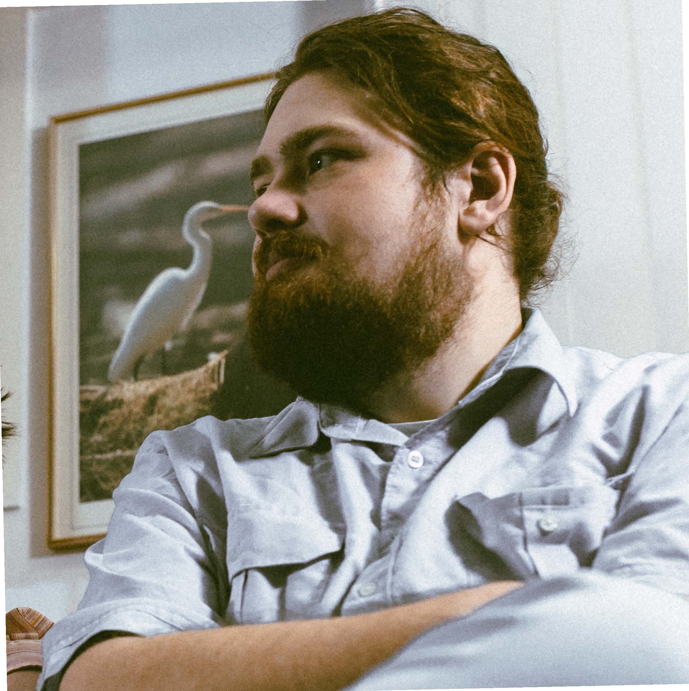 Man with hair pulled back and a beard looking off to the left off camera with arms crossed