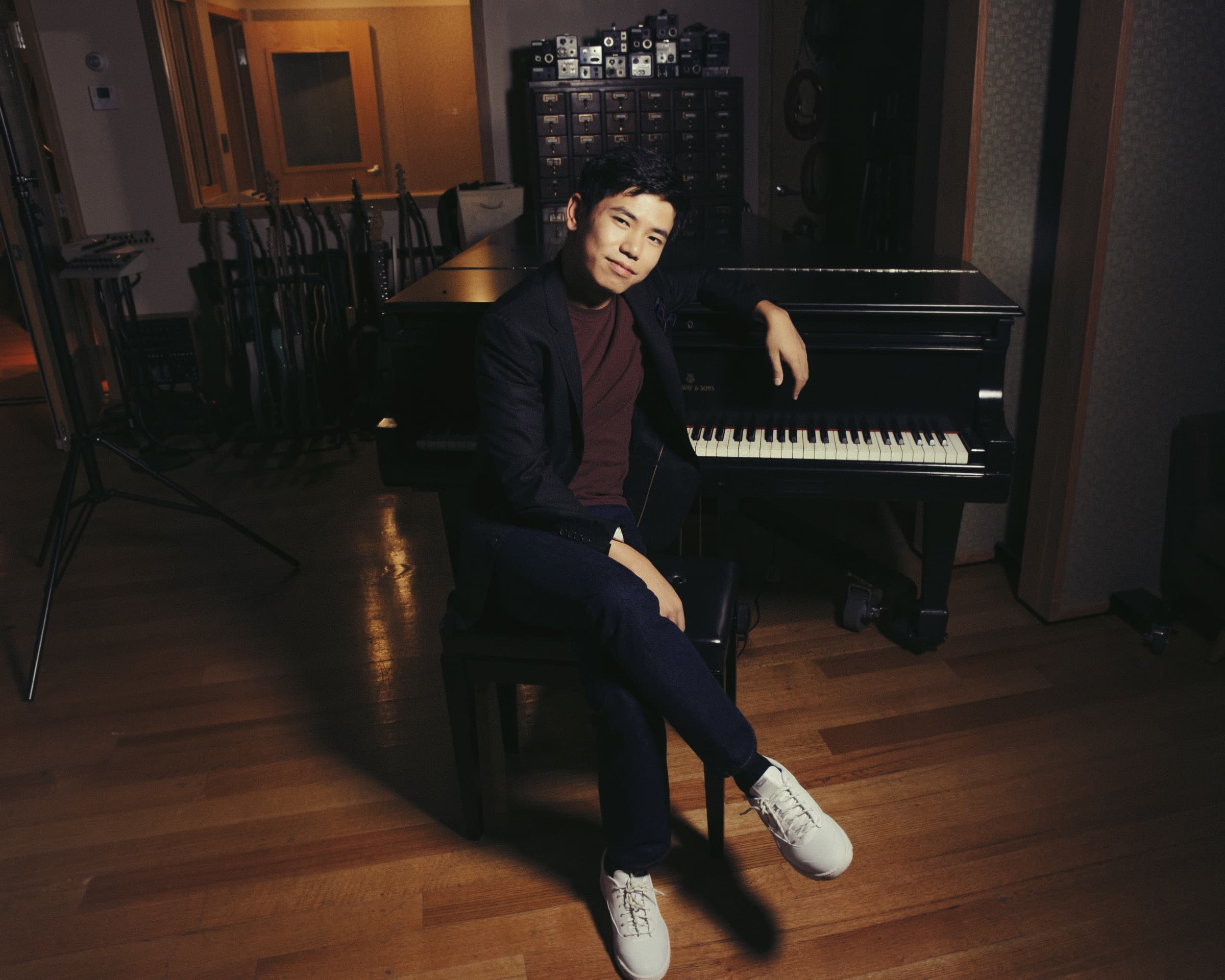 Man in black suit sat in front of piano looking at camera