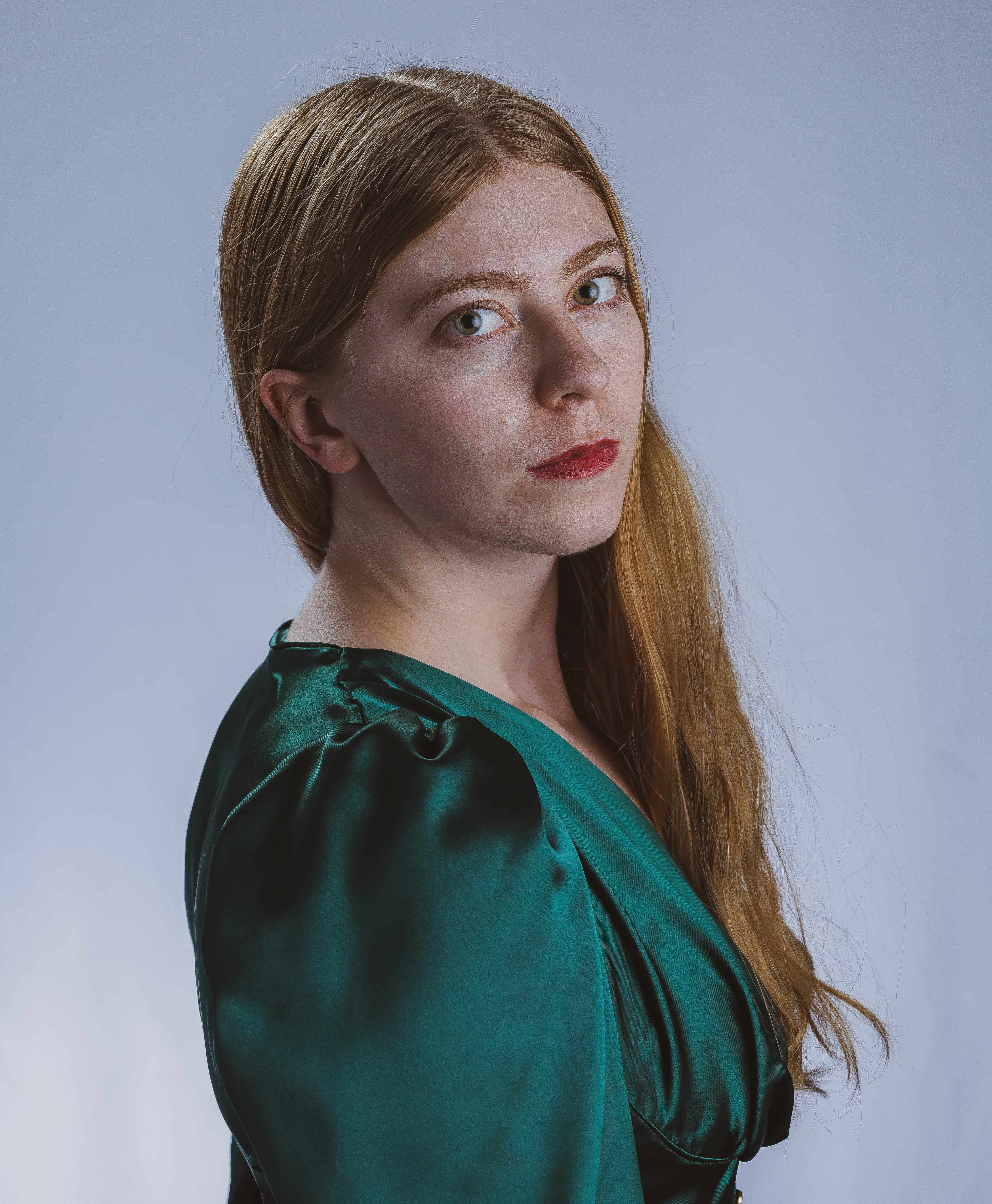 Woman with long red hair cascading over her shoulder, looking to the side directly at camera in bright green dress