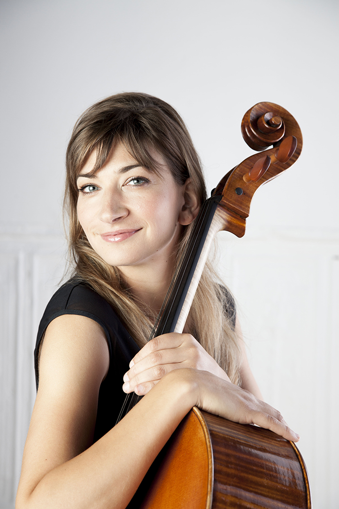 Cellist smiling at the camera with arms wrapped around cello