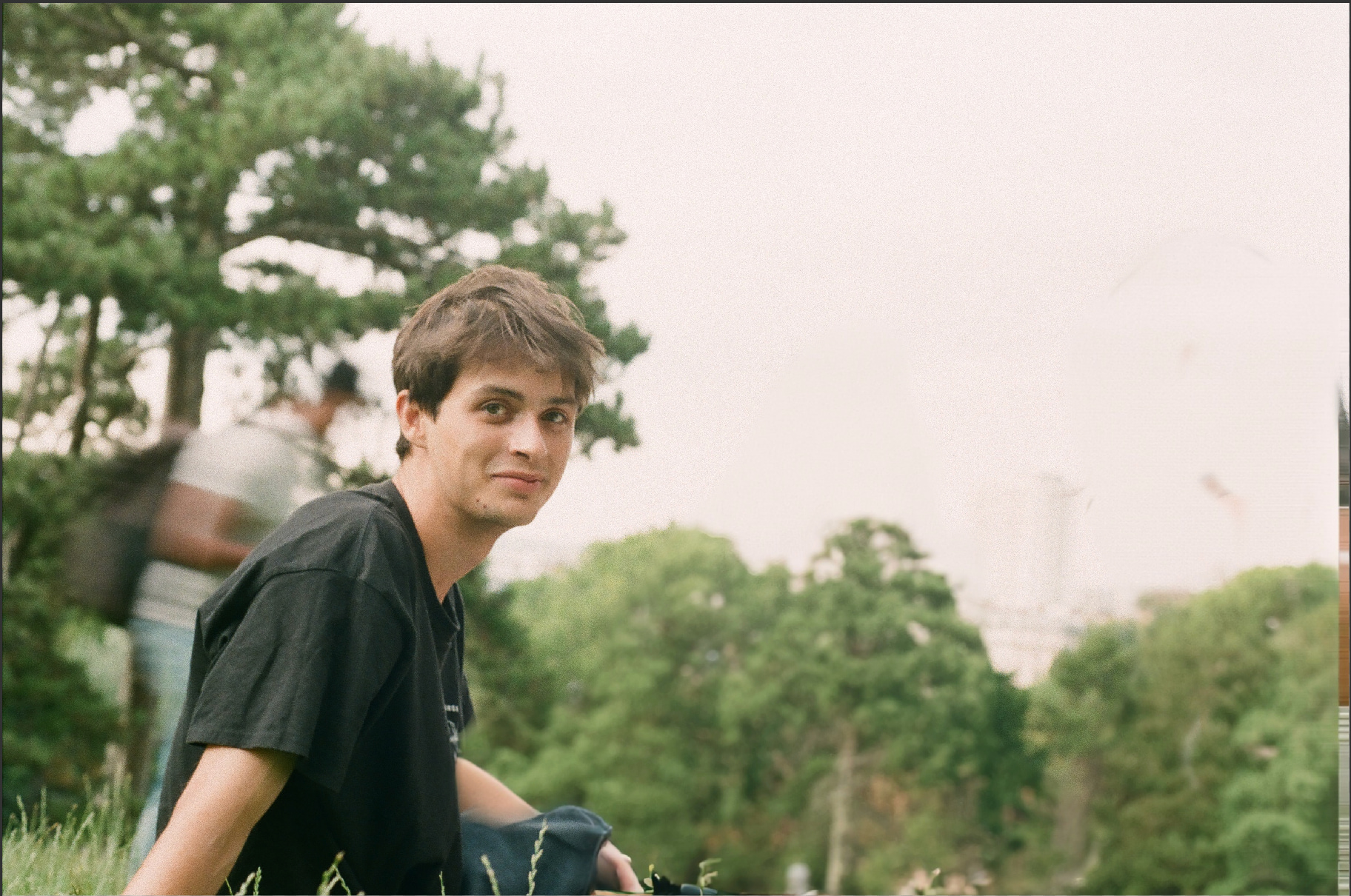 Casually dressed man sitting outside amongst trees looking at camera
