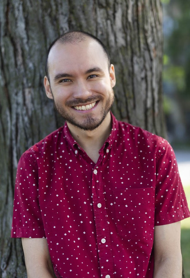 Man with red shirt and big smile leaning against tree