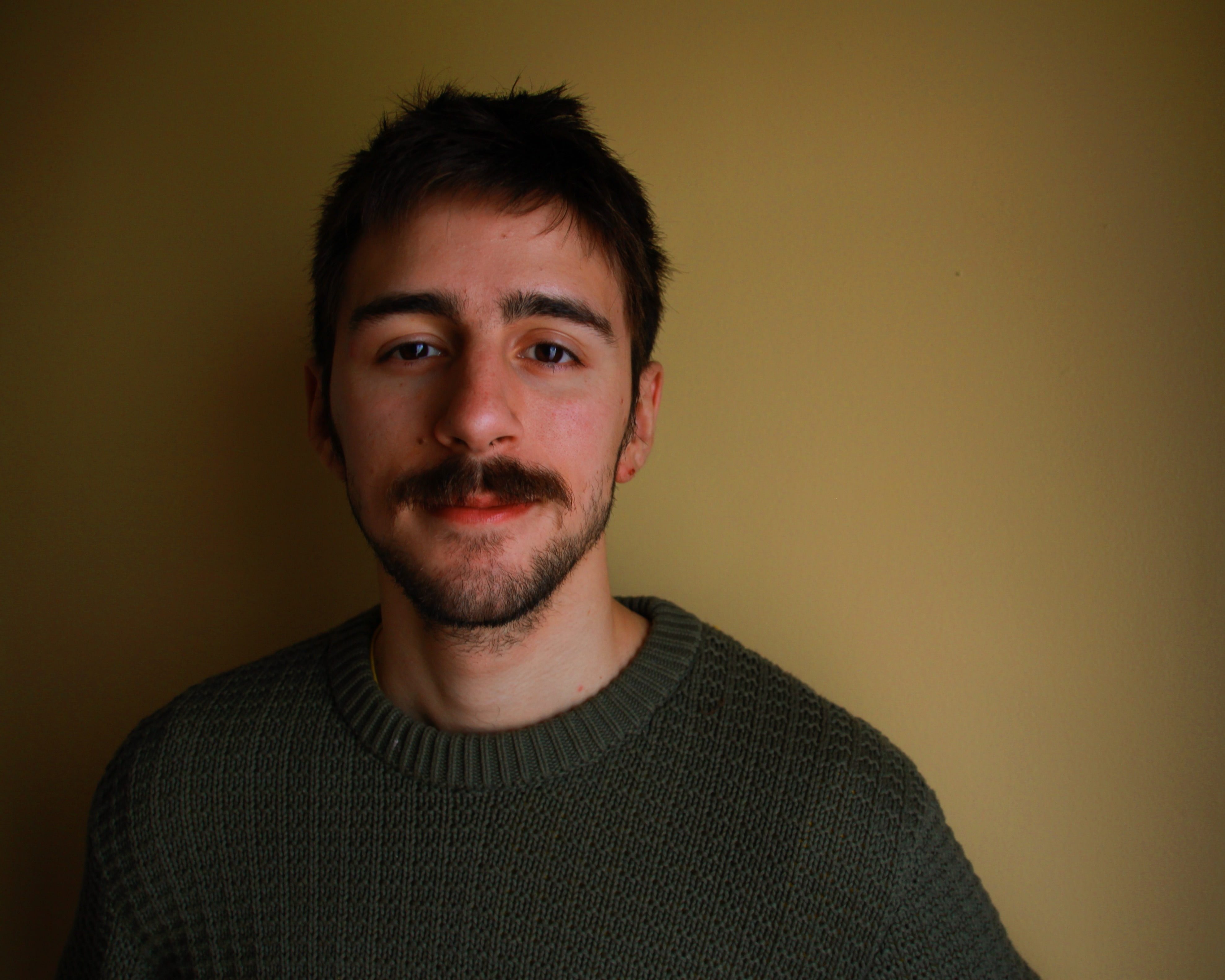 Man standing against wall in dark room smiling at camera