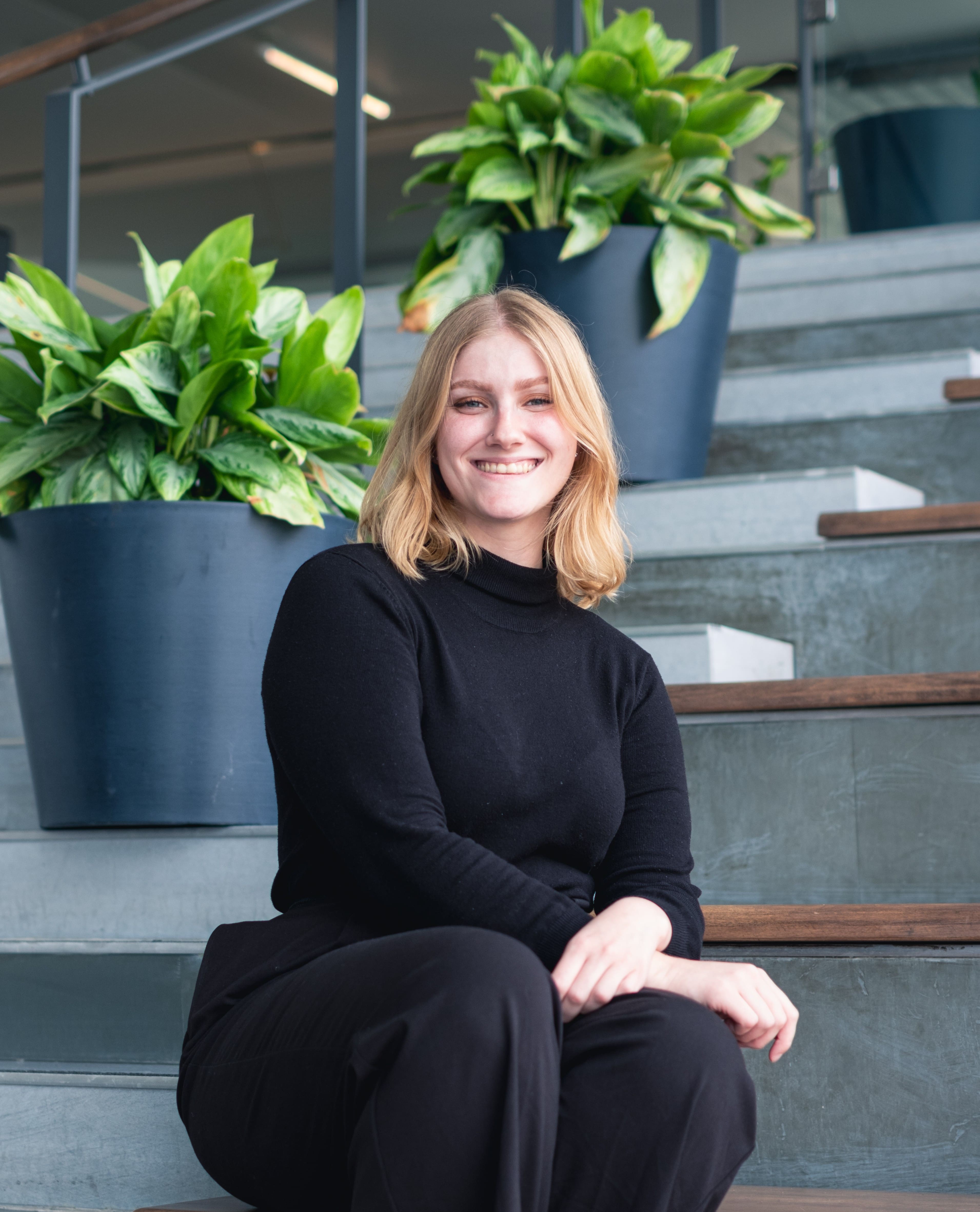 Woman sitting on stairs wearing all black smiling at camera