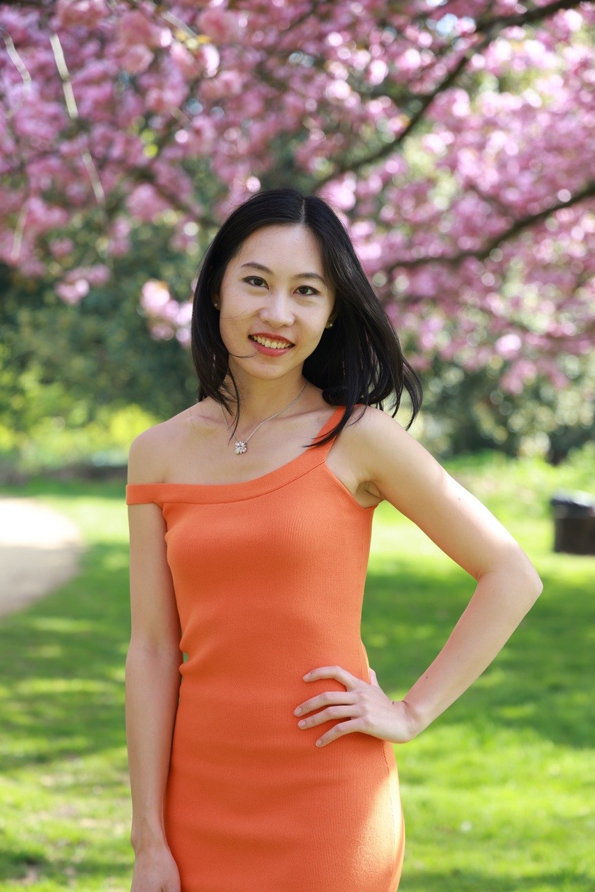 Woman standing confidently in bright orange dress in front of cherry blossoms