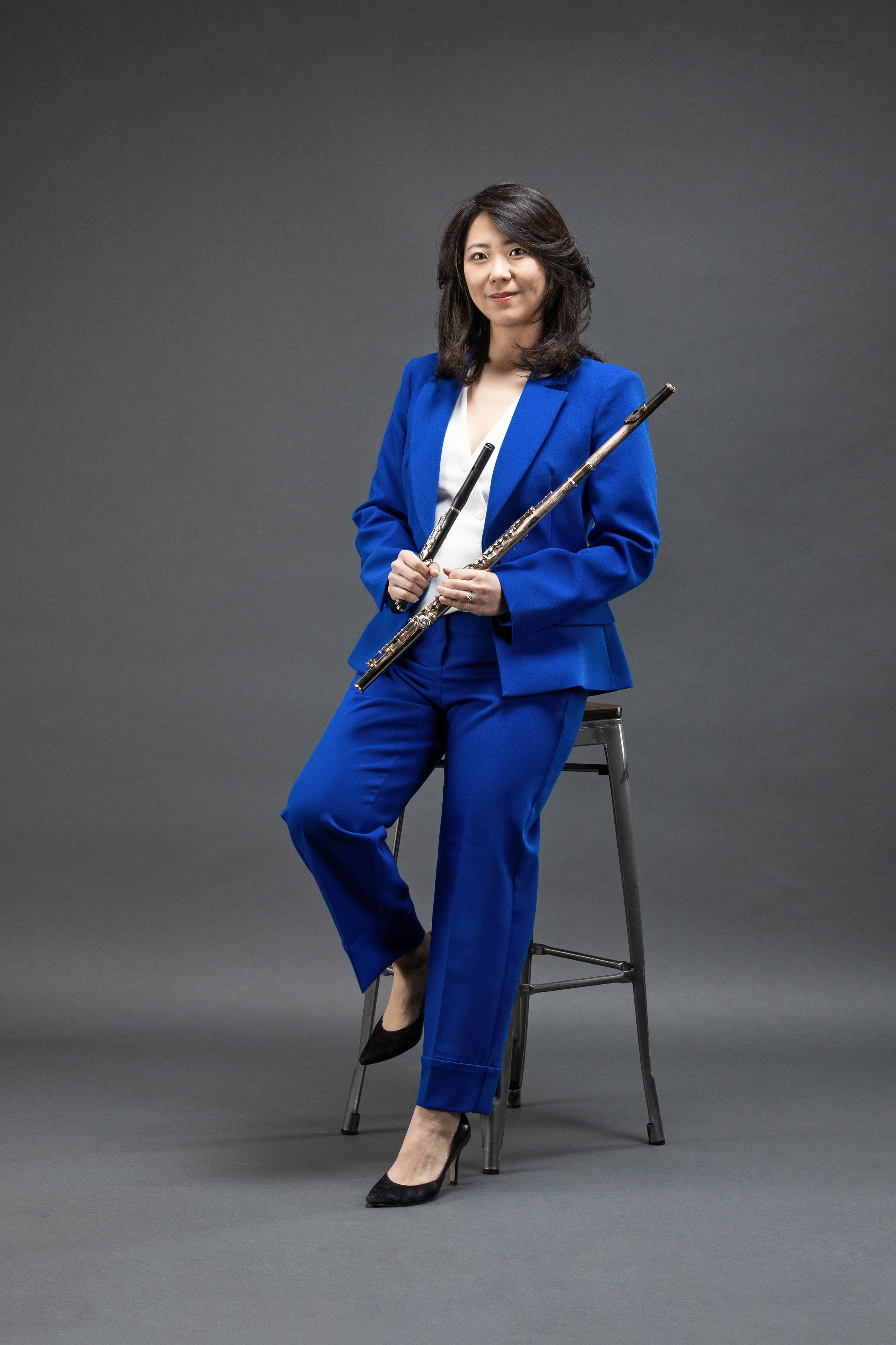 Woman in royal blue suit leaning against a stool holding instrument