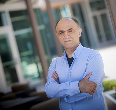 Man wearing blue button down standing outside with arms crossed in front of chest