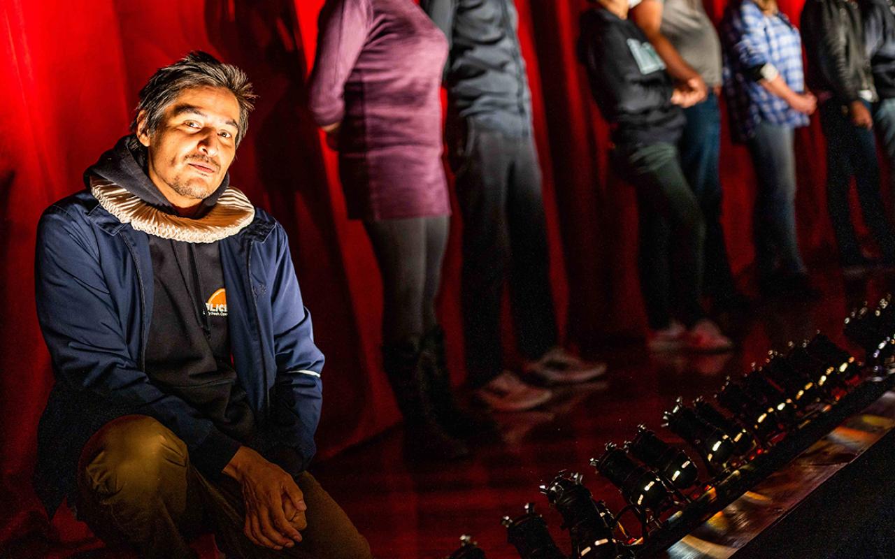 Photo of Cliff Cardinal kneeling on stage and looking at the camera