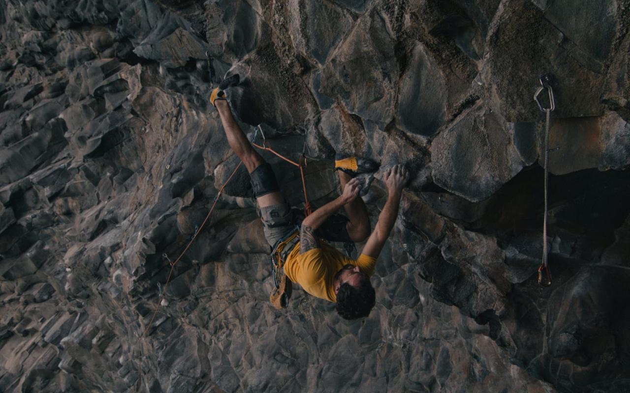 Man climbing on an overhang roof executing a challenging upside-down move with foot-hook.