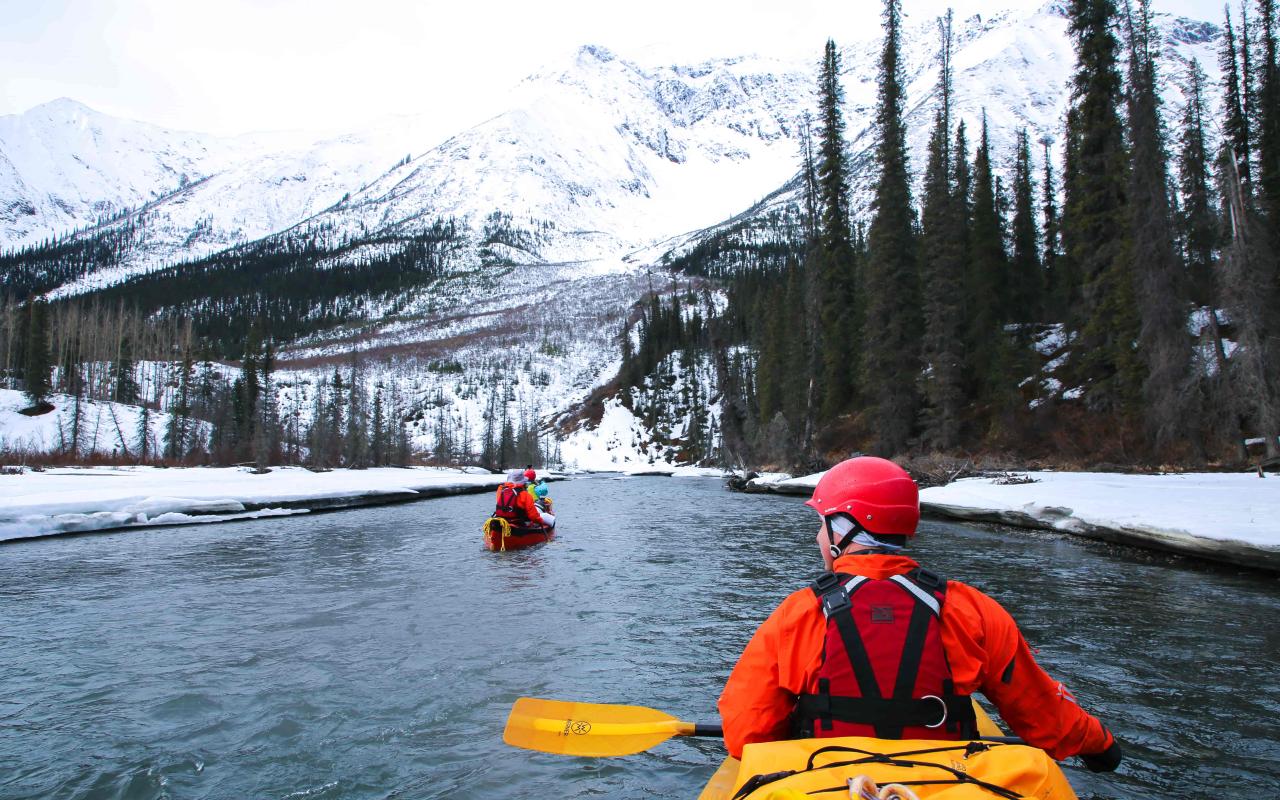 Kayakers on a river surrounded by snow and mountains