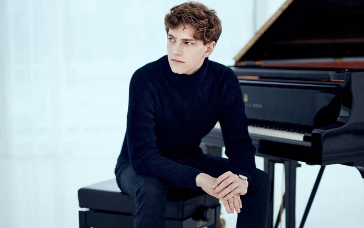 A man dressed in black is seated at a grand piano