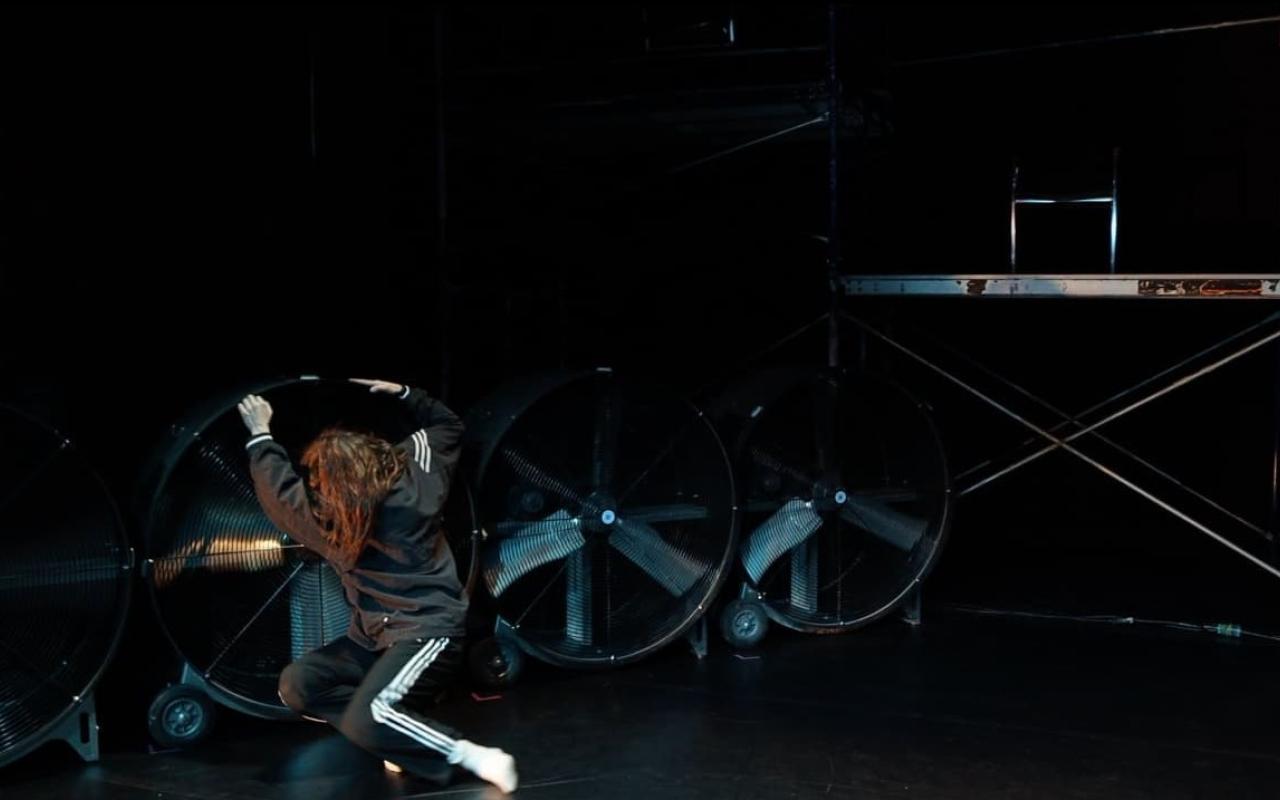 Photo of dancer on stage with industrial fans and scaffolding