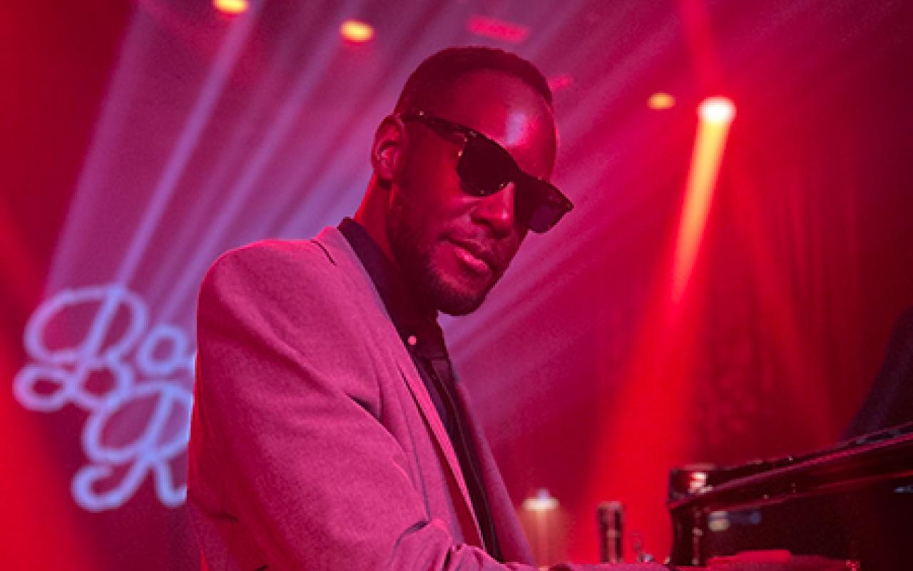 Timothonius wearing sunglasses playing the piano in dark club