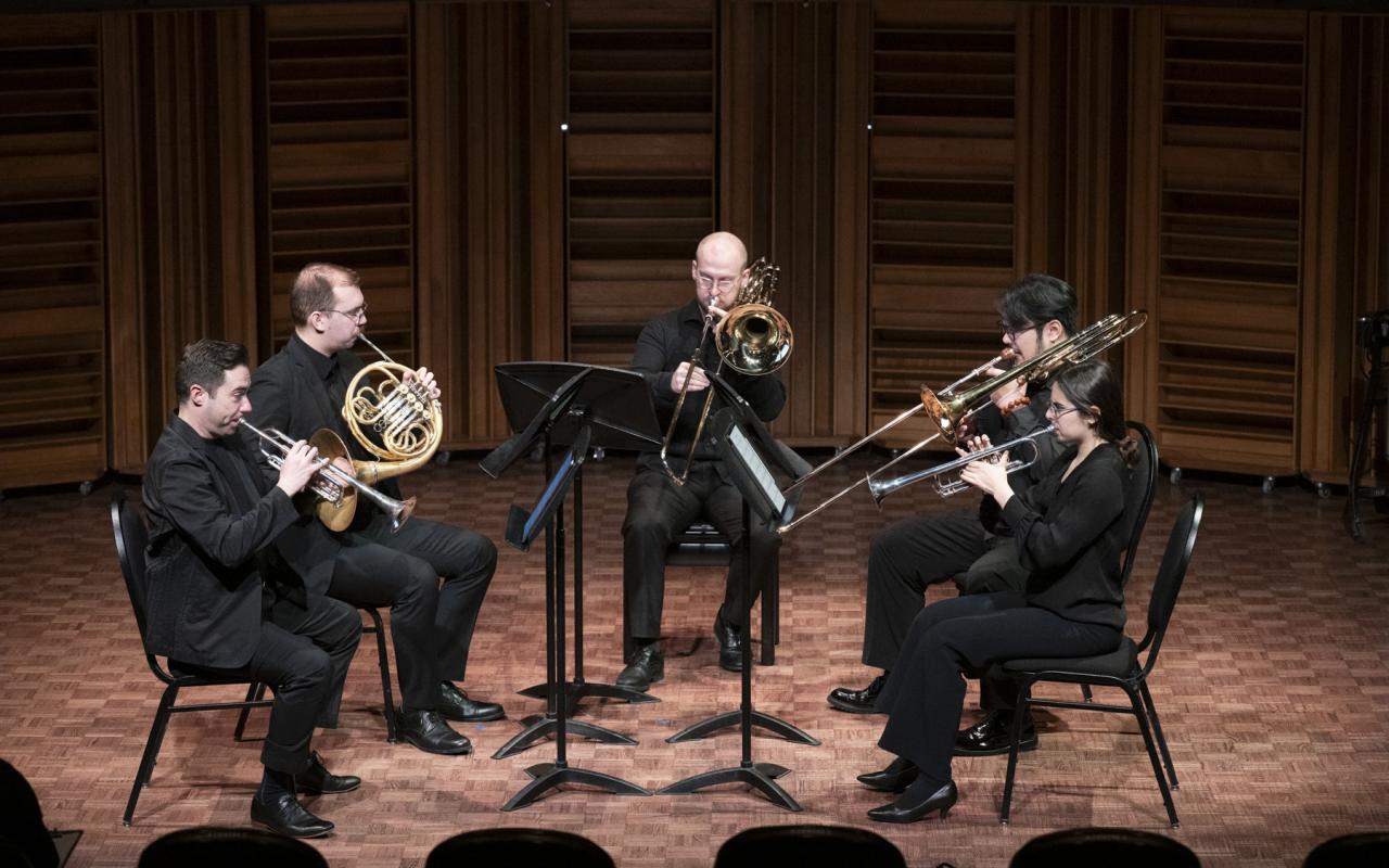 Chamber music group of 5 musicians on stage. Interplay Faculty and Participant Chamber Music Concert, 2025. L to R: Joel Brennan (trumpet), Tyrell Loster Peitzsche (horn), DJ Combs (bass trombone), Charlie Cao (trombone), and Fiona Shonik (trumpet)