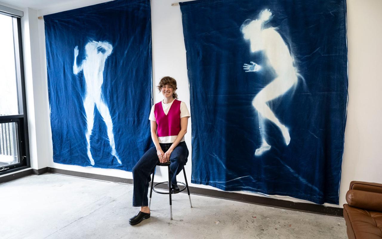 An artist is sitting in front of two large tapestries