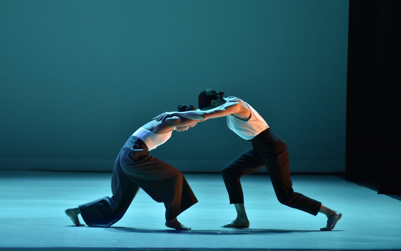 Dancers on stage holding each others arms and lunging toward each other