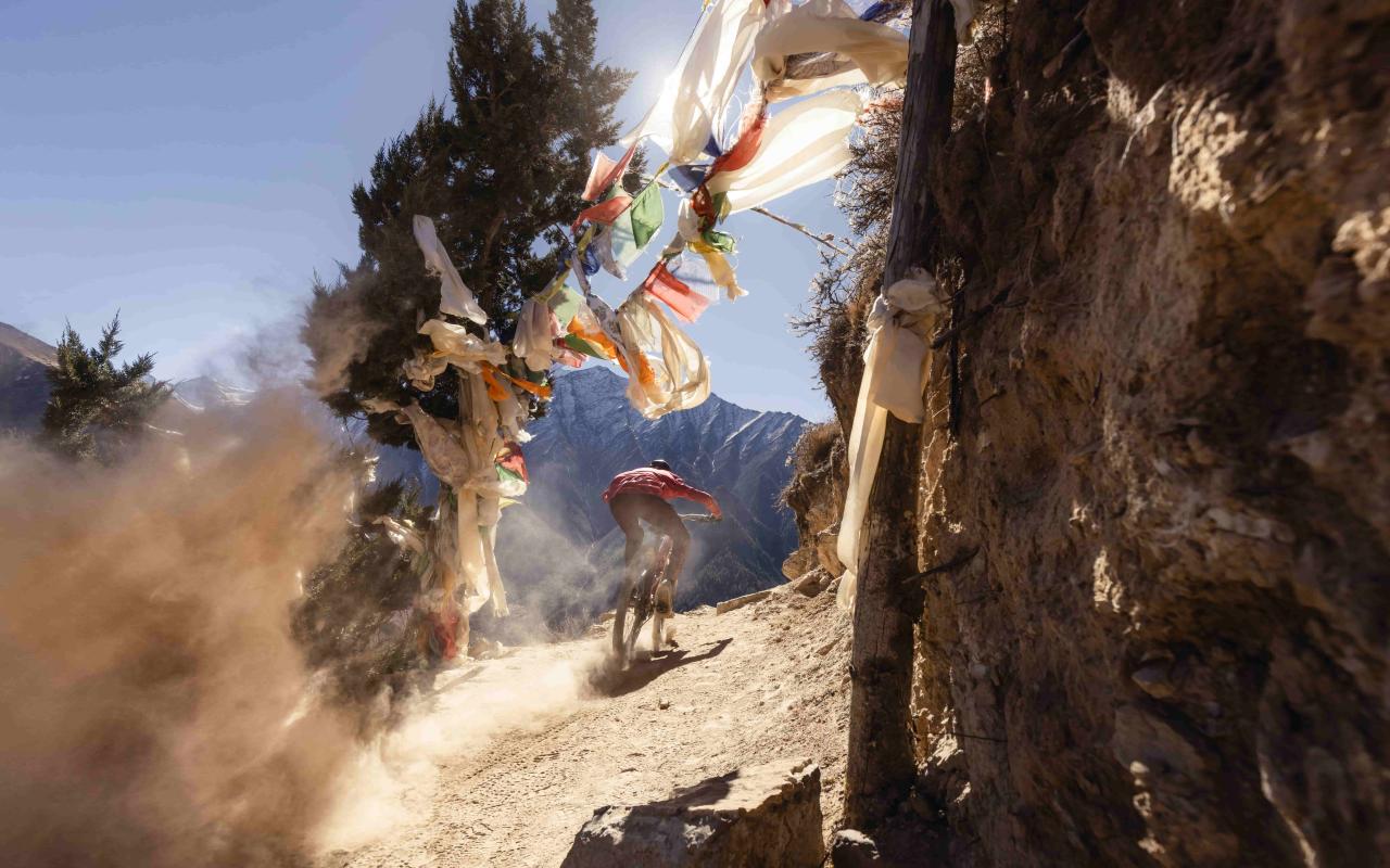 Biker speeding on a mountain road with Tibetan prayer flags hanging between trees and rocks