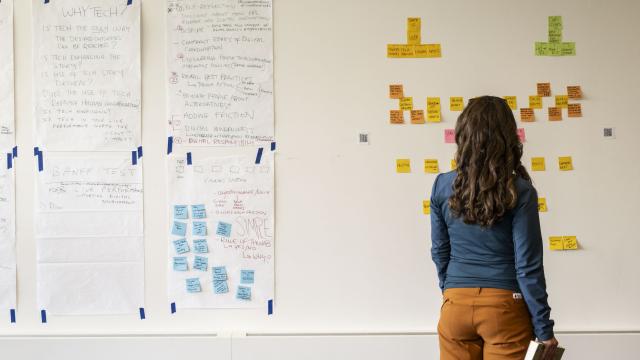 A woman stands in front of a blank wall covered in post-it notes