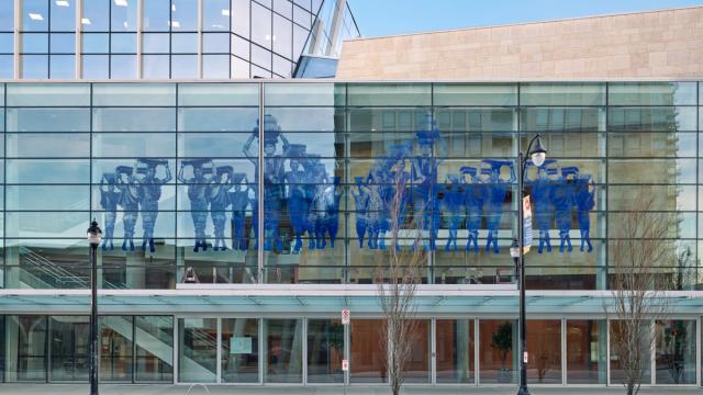 A photograph of many people in blue across a glass building