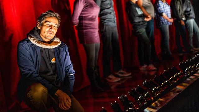 Photo of Cliff Cardinal kneeling on stage and looking at the camera