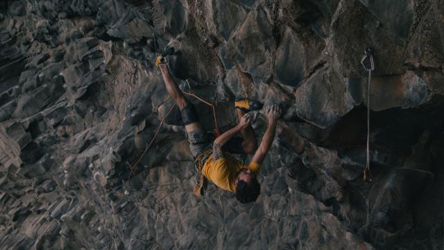 Man climbing on an overhang roof executing a challenging upside-down move with foot-hook.