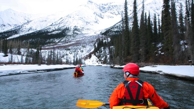 Kayakers on a river surrounded by snow and mountains