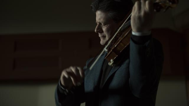 Barry Shiffman playing the violin in a dark theatre. 