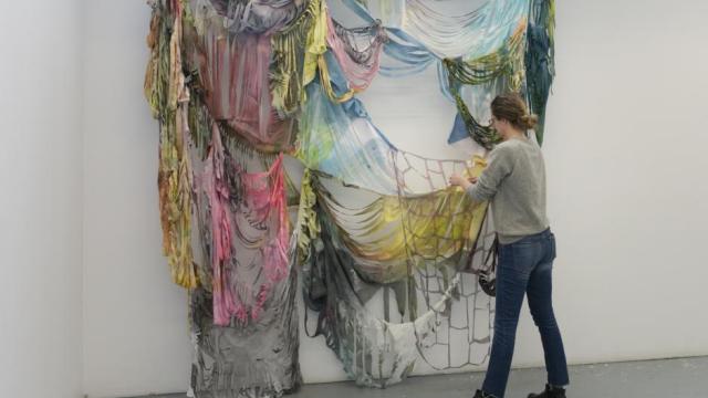 An artist manipulates multi-coloured fabric draped from a wall.