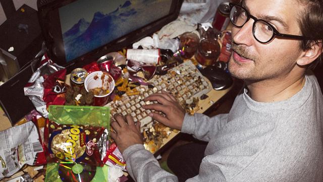 Visual Artist Jon Rafman sits with his hands on a filthy desktop and keyboard covered in fast-food items.