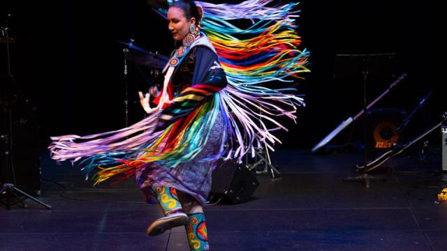 Indigenous woman in colourful ribbon regalia dances on stage
