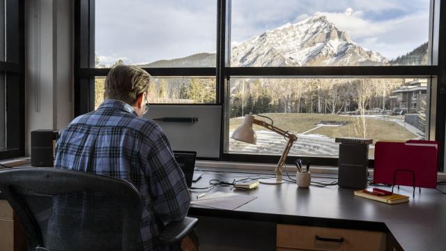 A writer is sitting at a desk in front of a window with a mountain view