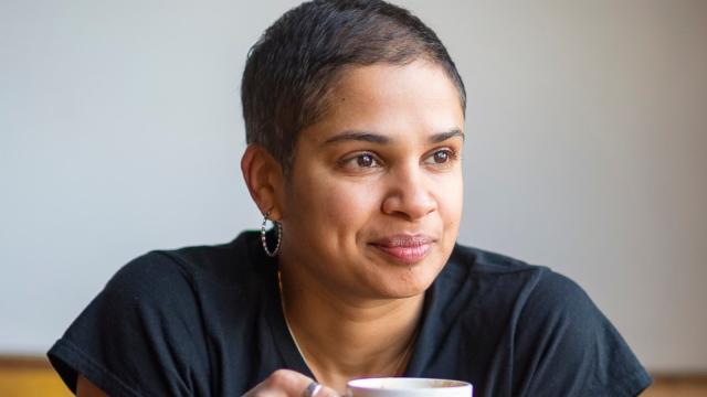 Photo of program faculty, Tanya Boteju, relaxed and smiling, leaning forward with coffee mug held in both hands