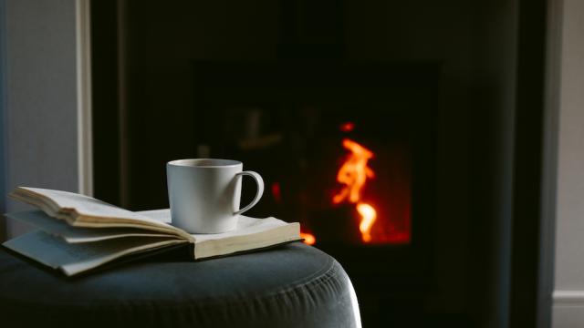 Cup of coffee on an open book in front of a fireplace.