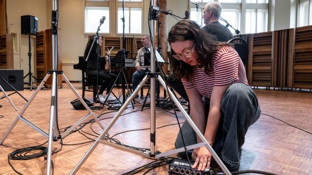 An audio engineer is kneeling on the floor to adjust audio cables