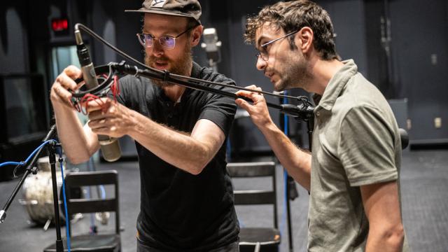 Two audio engineers are adjusting a microphone stand in a studio