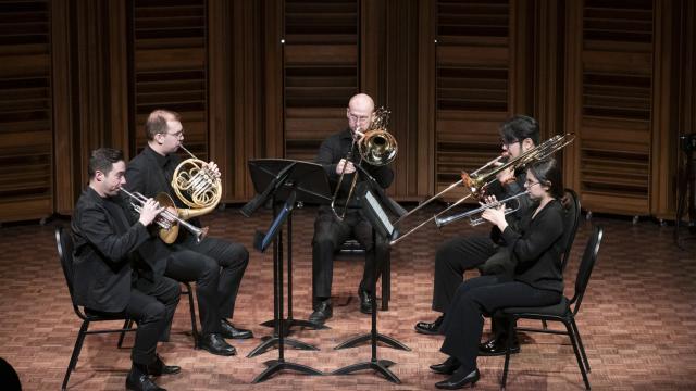 Chamber music group of 5 musicians on stage. Interplay Faculty and Participant Chamber Music Concert, 2025. L to R: Joel Brennan (trumpet), Tyrell Loster Peitzsche (horn), DJ Combs (bass trombone), Charlie Cao (trombone), and Fiona Shonik (trumpet)