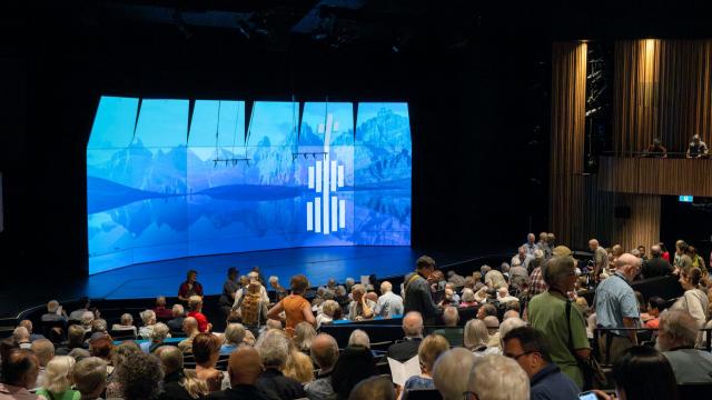 Interior Jenny Belzberg Theatre - Packed Audience in front of empty stage and blue screen with BISQC logo
