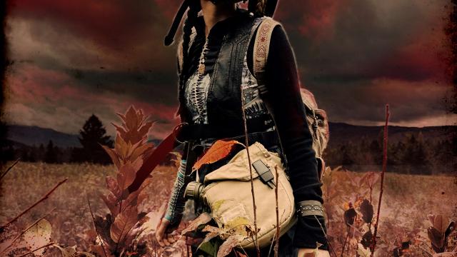 Woman standing in a field with dark, red sky and red tinted landscape. Woman wears gas mask, goggles and carries a large