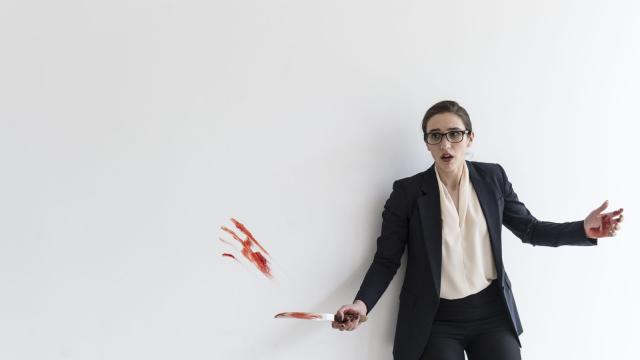 A woman stands surprised against a white background with blood on the knife and wall