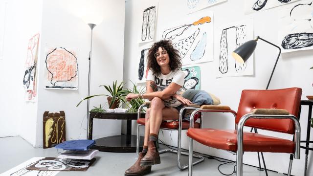 Artist Laura Jean Foster is seated in a studio in Glyde Hall, surrounded by her art