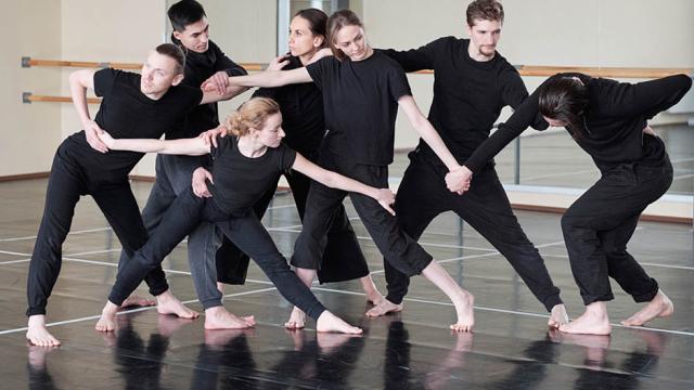 A group of dancers dressed in black clothing are practicing a routine