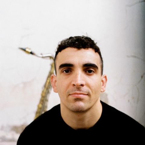 Man with short hair smiling at camera with saxophone in the background