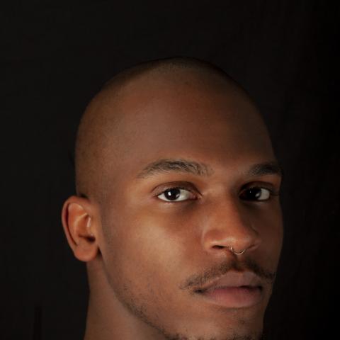 close portrait of man looking directly at camera against dark background
