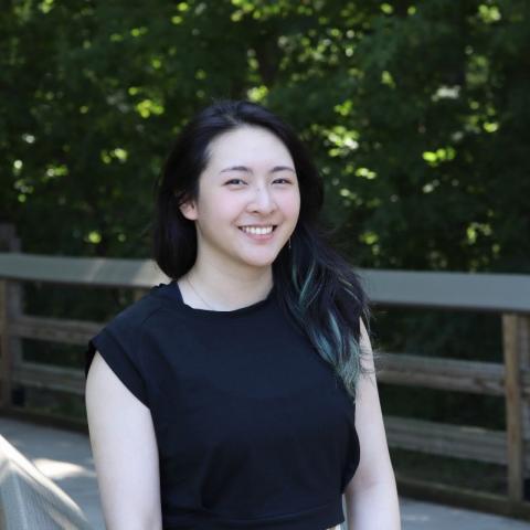 Smiling woman with dark hair posing by a wooden fence.