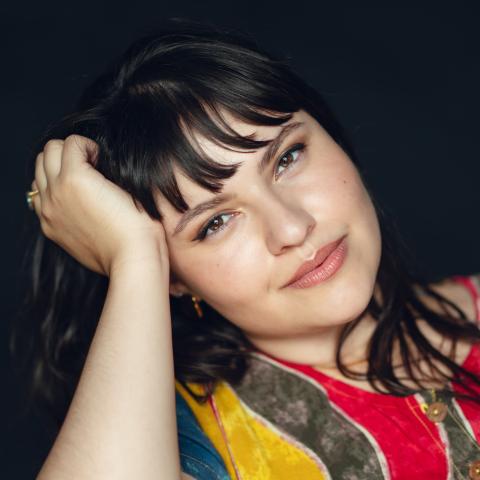 Woman wearing colourful shirt holding head up with hand looking directly at camera
